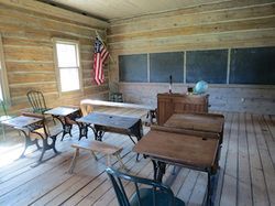 A historical classroom with wooden furniture, blackboards, and an American flag.