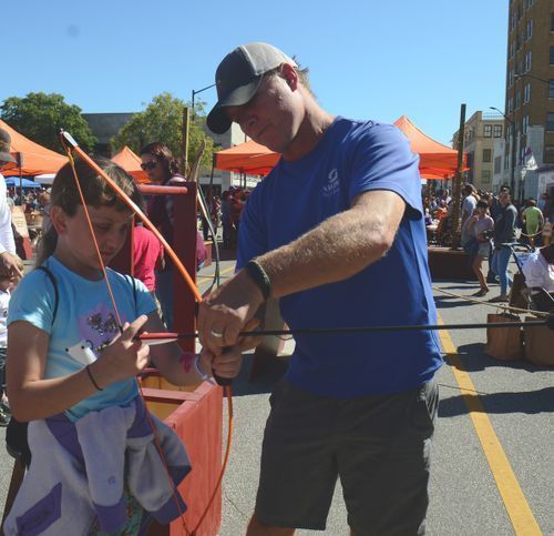 Smoky Hill Museum Street Fair volunteer showing a teenage girl how to shoot a bow and arrow.