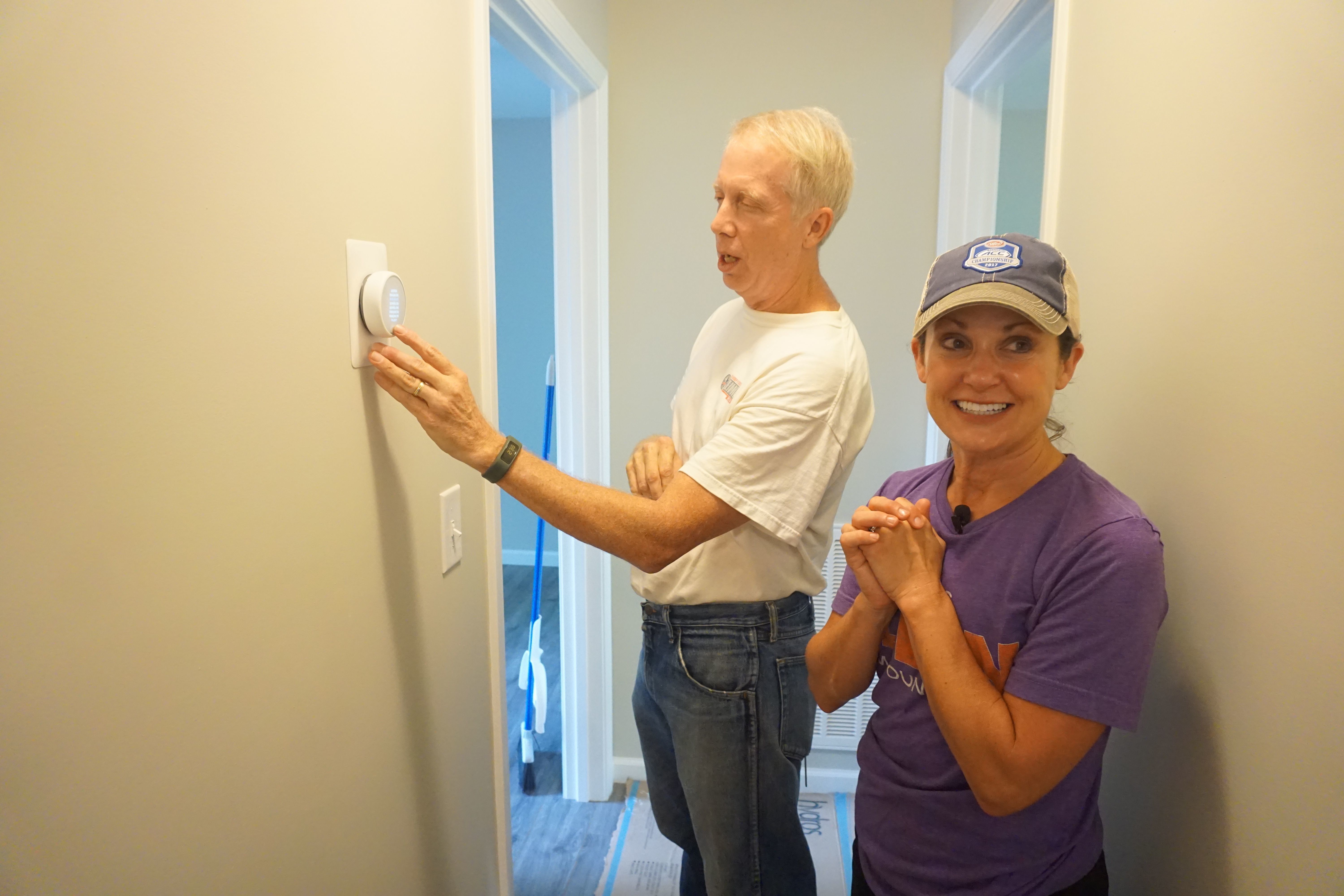 Vice Chair of All In Foundation Kathleen Swinney clasps her hands together as volunteer Worth Henley prepares a thermostat.
