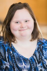 Professional headshot of white woman with Down syndrome smiling at camera