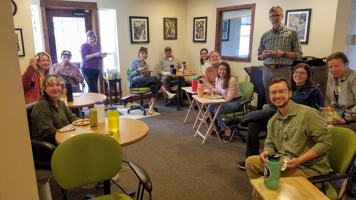 [Image Description: Bozeman State staff sit in a circle while eating pizza for a birthday celebration.]