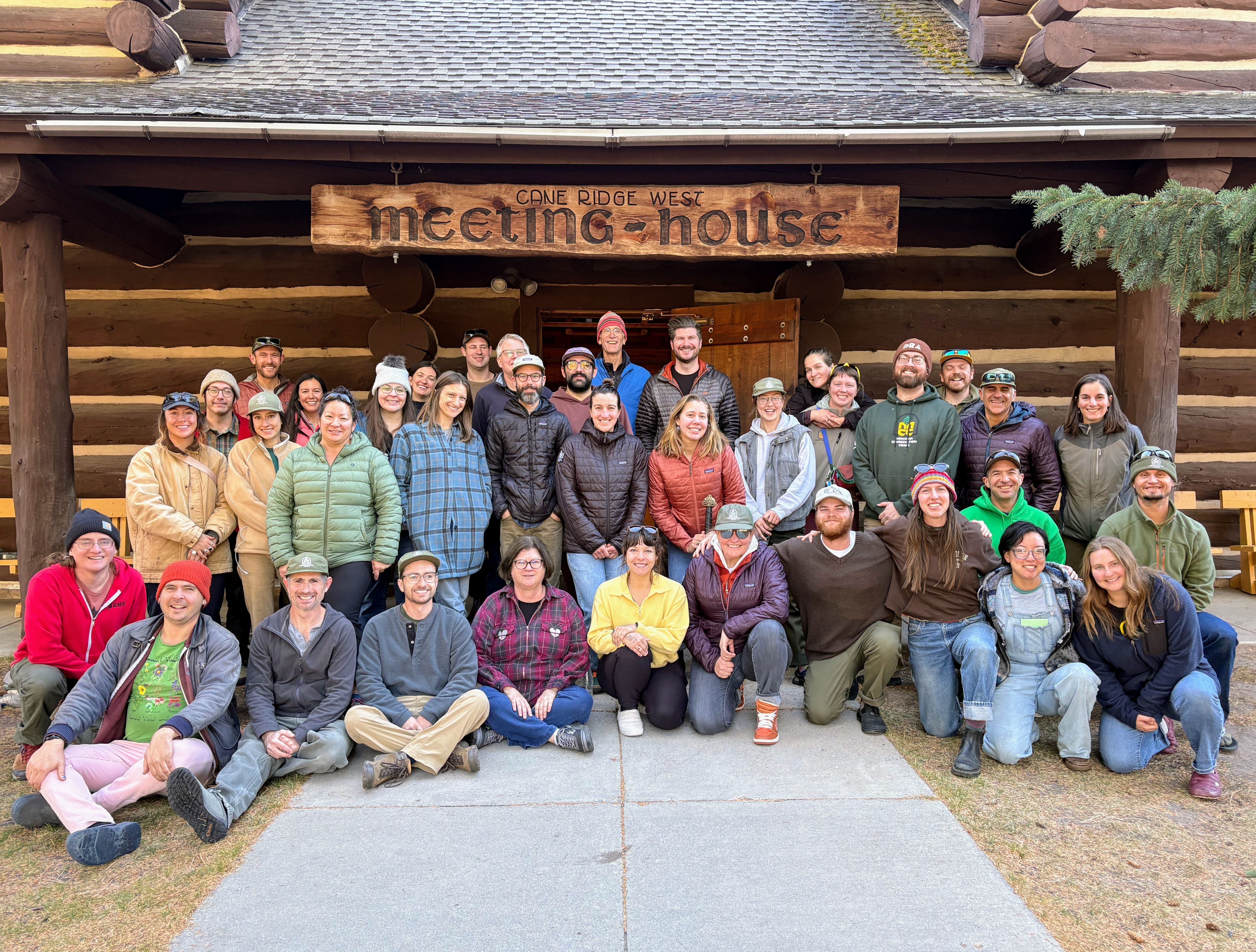 [Image Description: MCC staff stands together in front of a log cabin.]