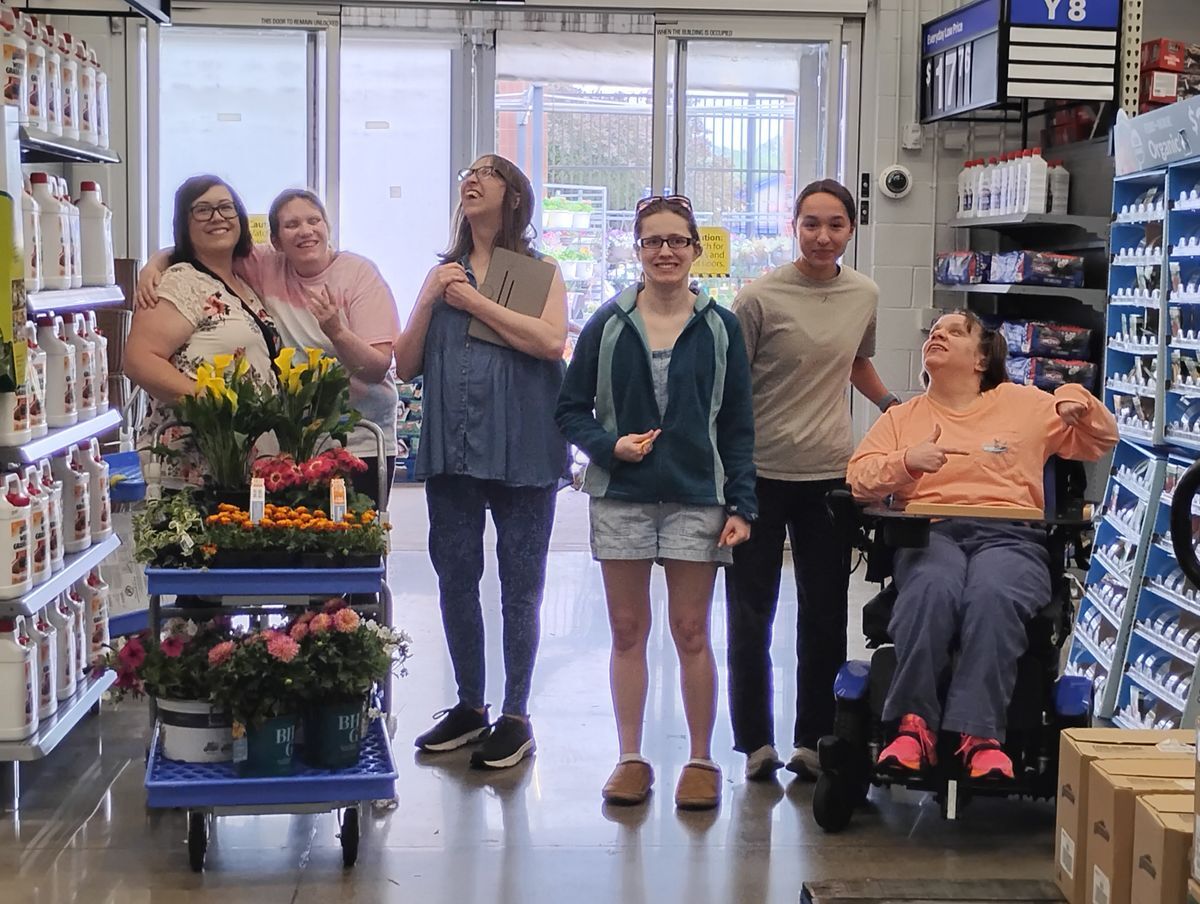 Six people standing in a straight line in the middle of the Walmart garden center, smiling and plants in the cart.