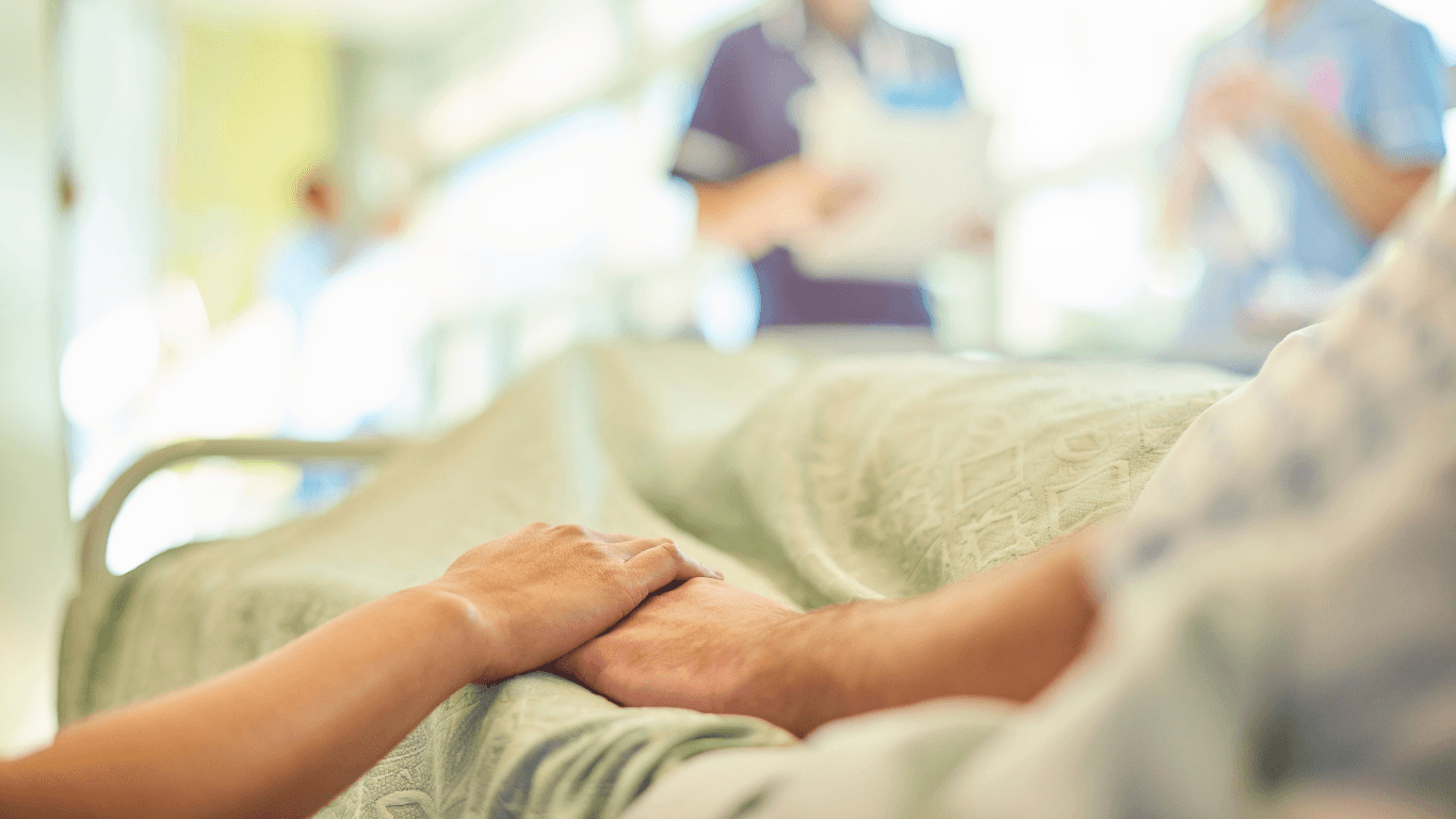 Two people hold hands in a hospital while a doctor looks at a clipboard