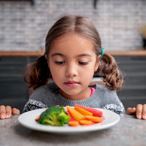 Child seated at table with plate of food.