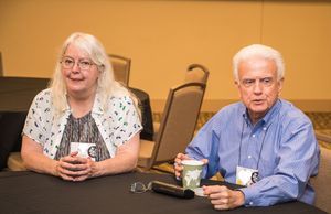 A woman and a man, both with grey hair, are sitting side by side at a round table. 