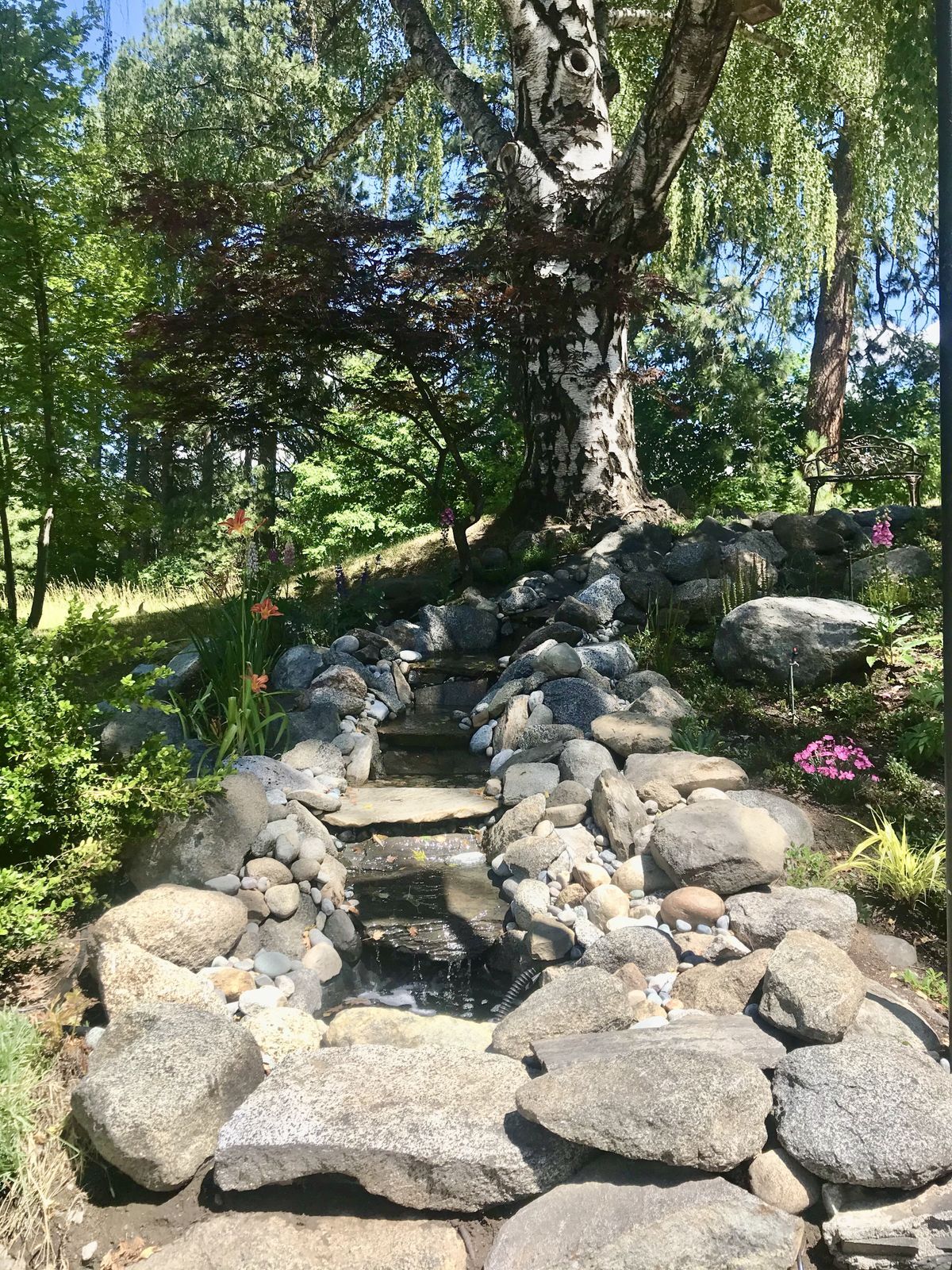 A rock garden with a waterfall flowing, with flowers and greenery bordering it.