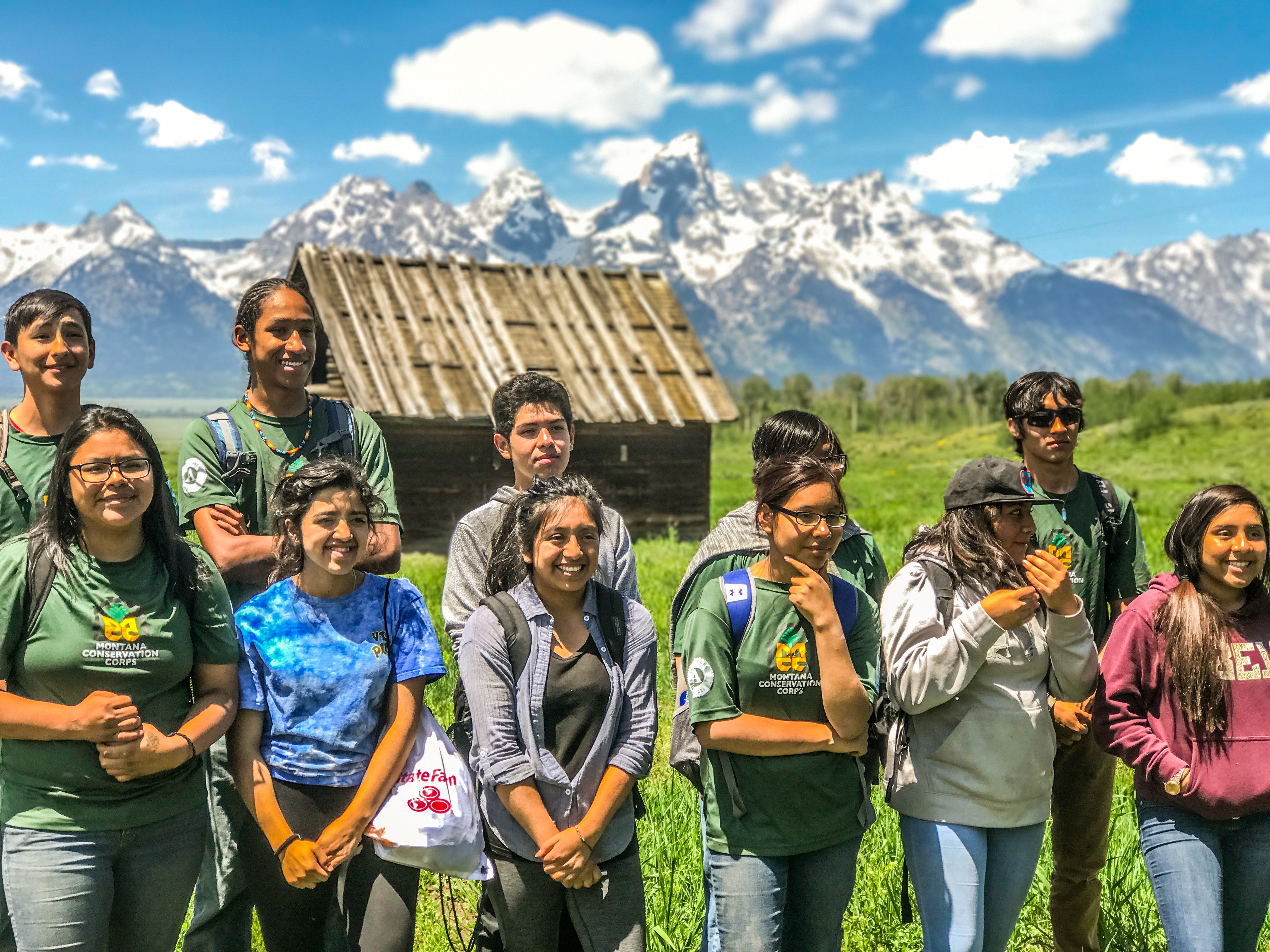 [Image Description: Eleven MCC Members standing together smiling, with a barn and the Teton Mountain Range in the background.]