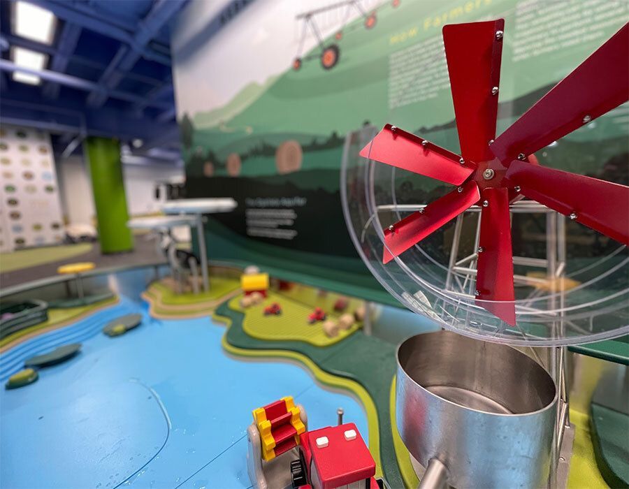 Educational agricultural display featuring a model wind turbine with red blades and a miniature farm scene.