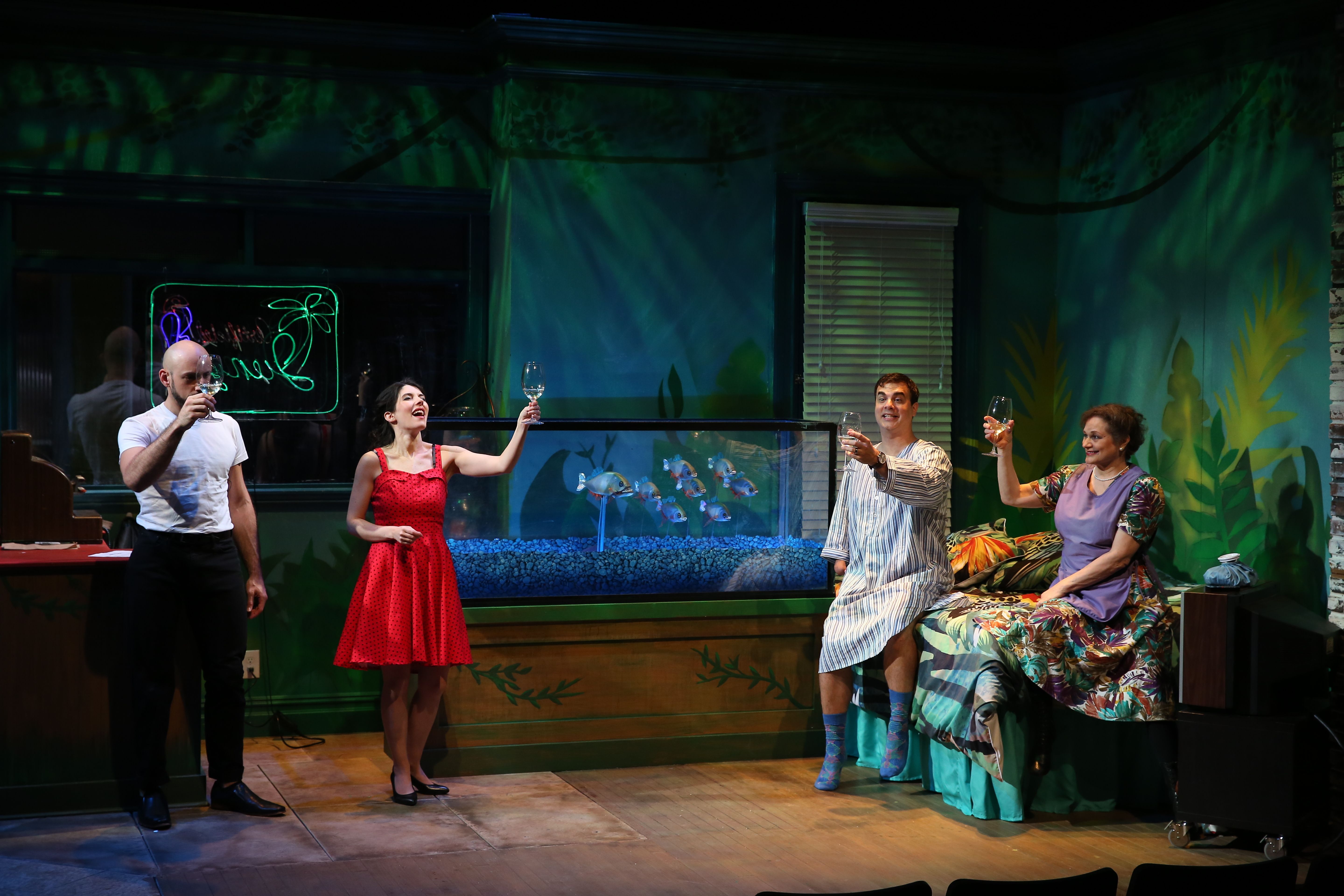 A picture of a group of actors who are standing and performing a scene from The Artificial Jungle. They all are holding wine glasses and making a toast. They are all smiling in the picture.