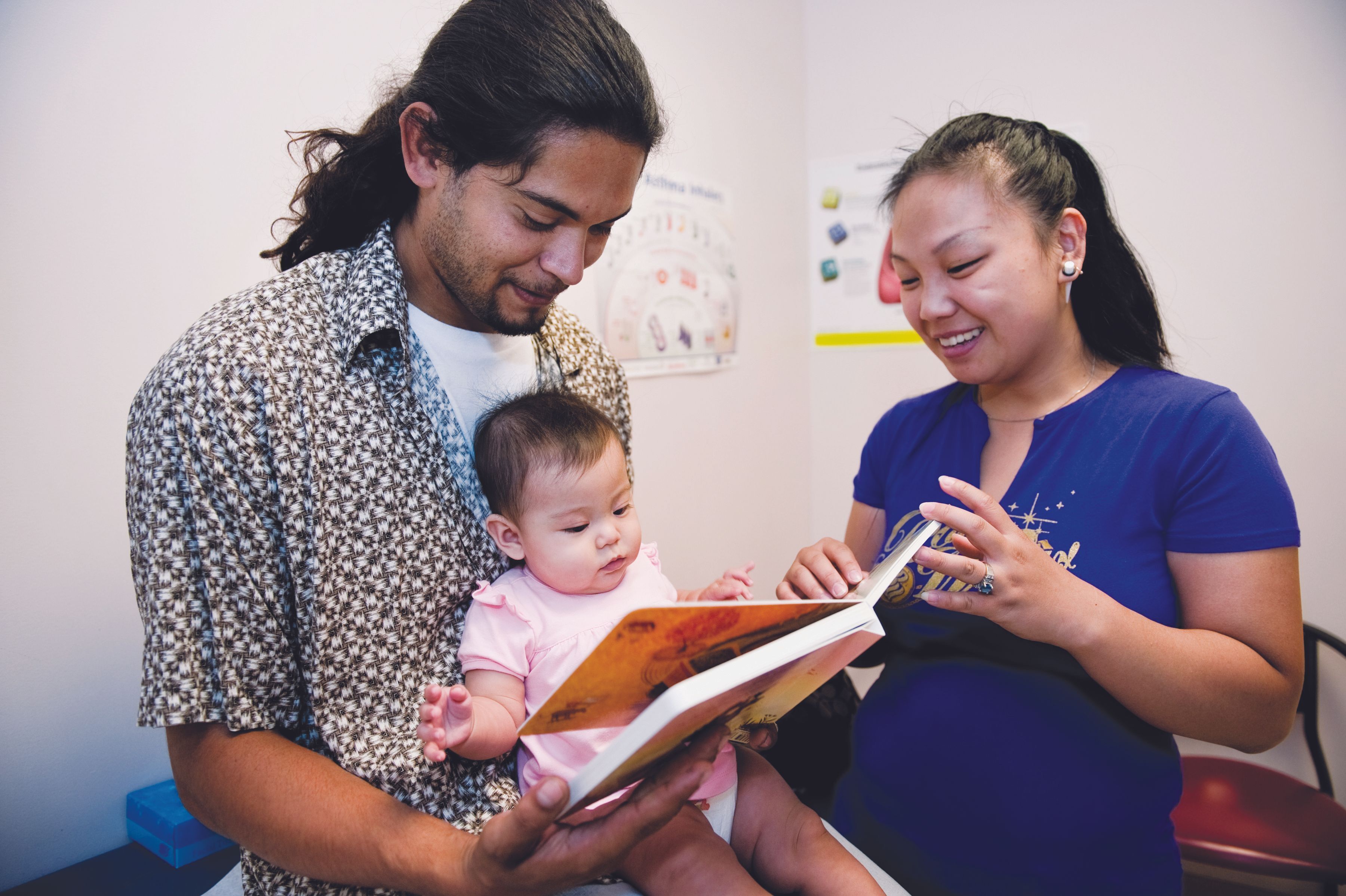 Father, infant, and mother look at book together