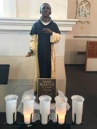 A statue of a man draped in cloth, with a plaque that reads "Saint Martin de Porres"