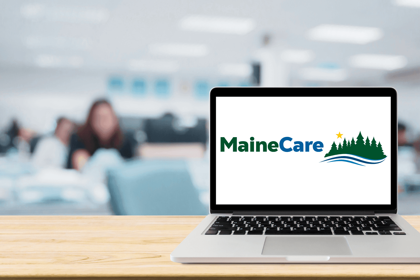 An open laptop in the foreground displays the MaineCare logo in blue and green while CAHC HelpLine advocates take phone calls in the background