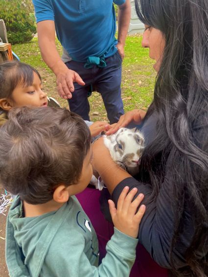 A woman on the right holds a large bunny rabbit and two children to the left gather around her to pet the bunny.