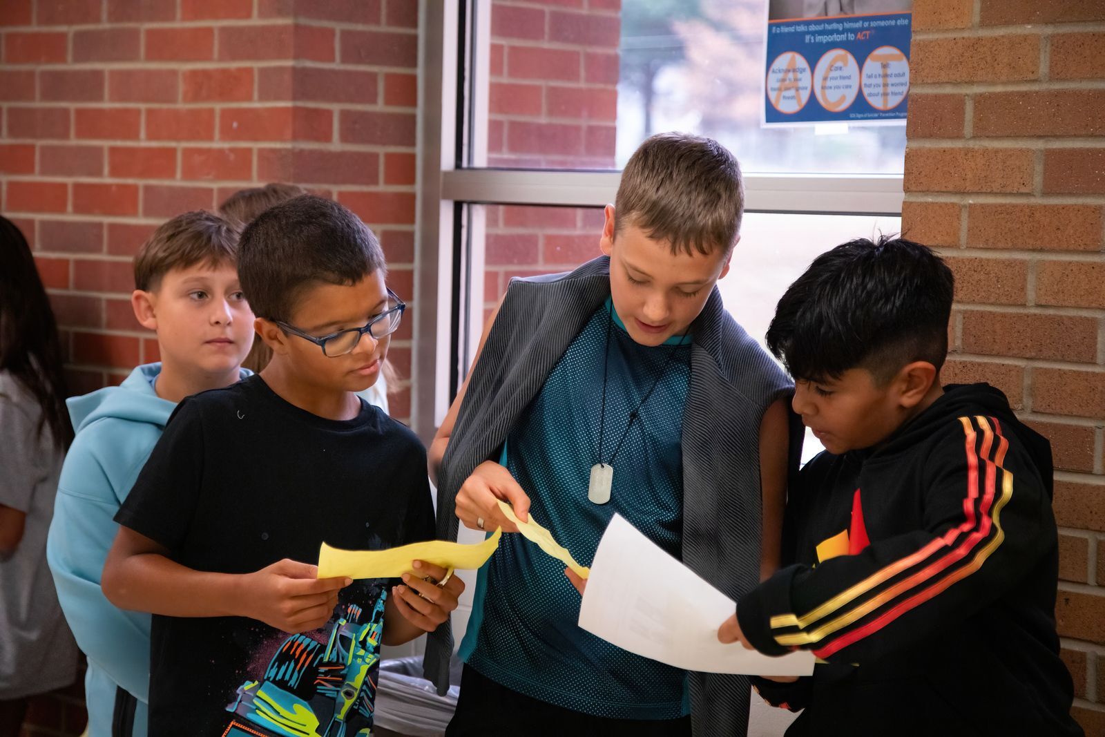 group of 3 middle school aged boys looking down at a sheet of paper in school hallwy