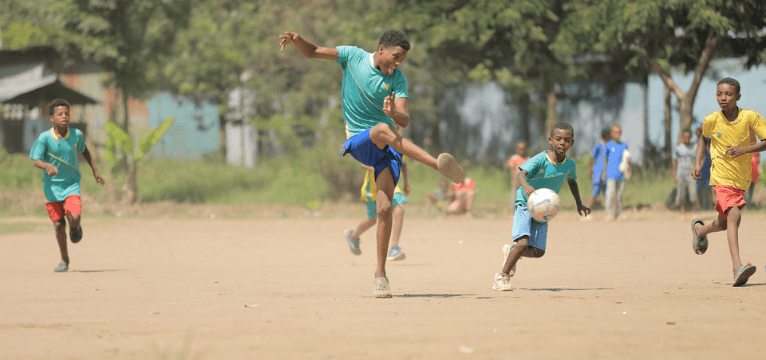 Roots Ethiopia school team photo with boys in uniform playing a friendly match of soccer on a dirt field at their school. 