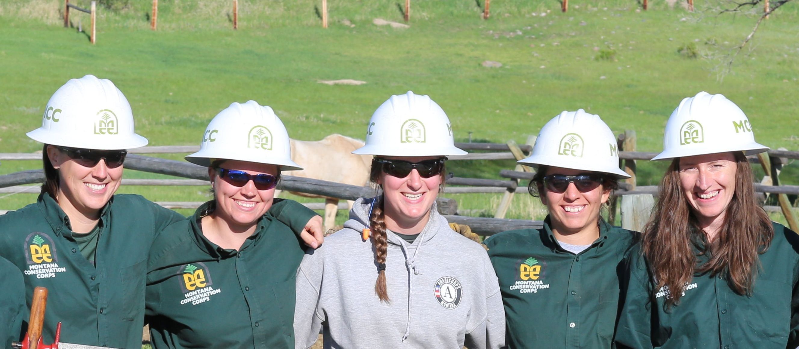 [Image Description: Five MCC members standing together smiling, all wearing MCC shirts and hard hats in front of a horse corral, with one horse behind them.]