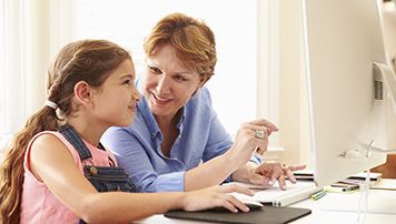 Woman teaching a girl to use a computer.