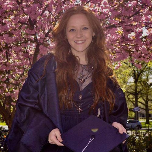 young woman in a graduation gown standing in front of a flowering tree