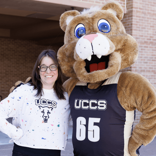 Clary wears a white UCCS shirt and has her arm around Clyde, the UCCS mountain lion mascot.