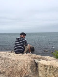 Photo of Brian Switzer sitting on a rock with a view of the ocean behind him