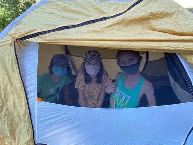 Three campers wearing masks looking out tent window.