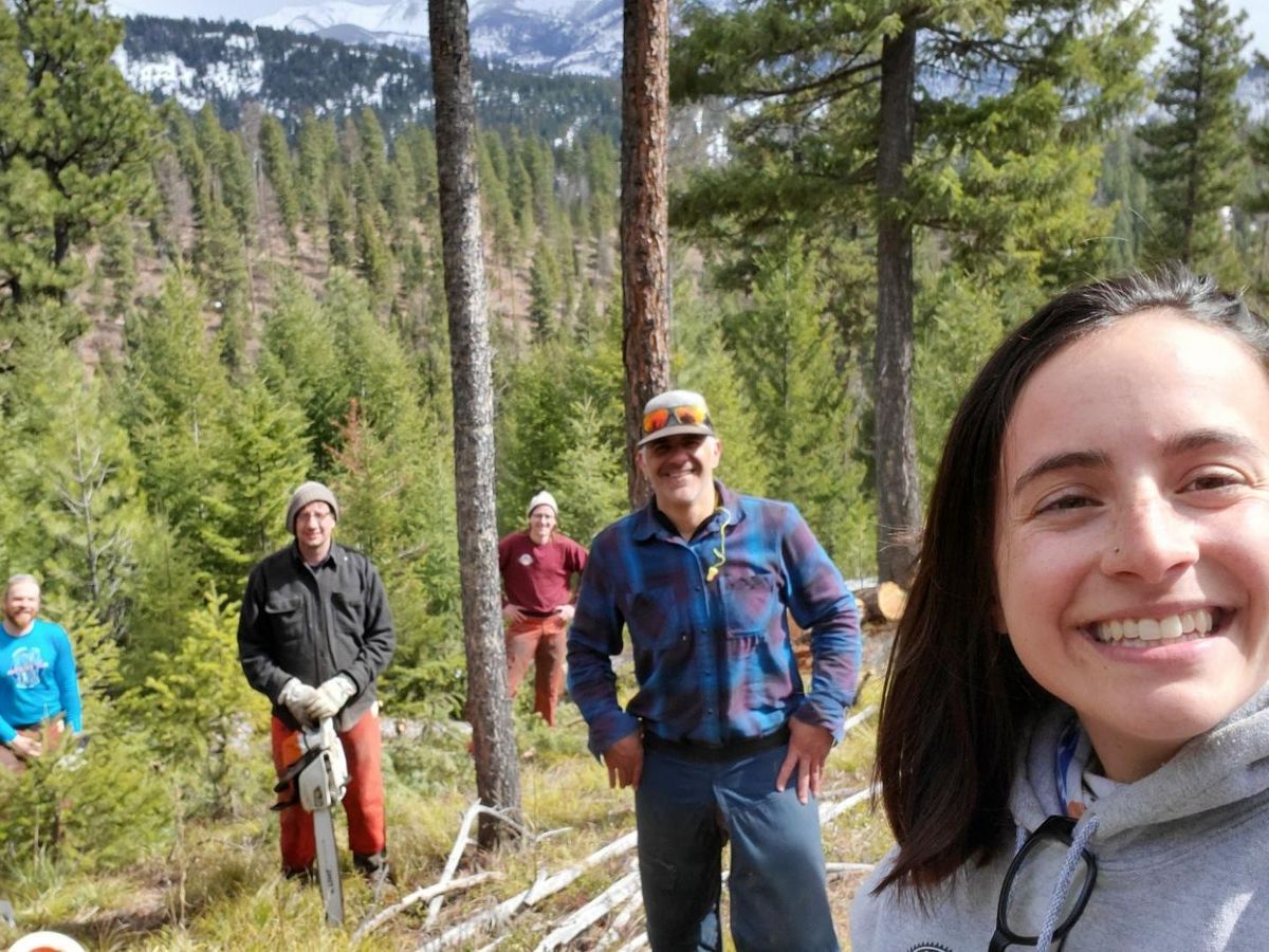 [Image Description: Staff members all pictured smiling, standing on a hillside filled with old growth trees and one chainsaw.]