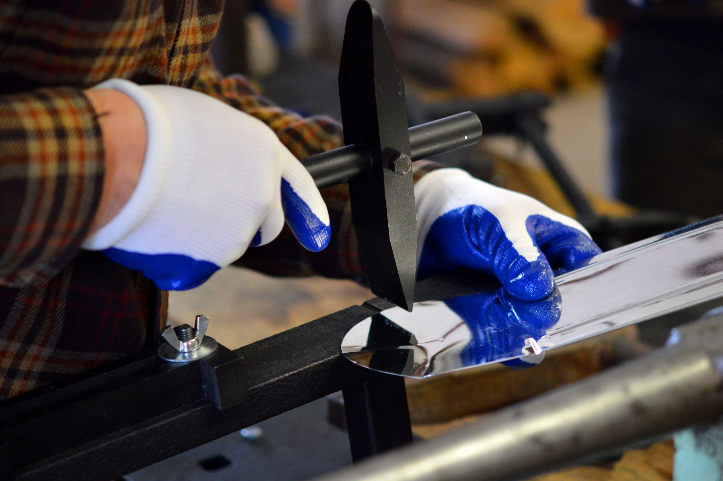 Close up photo of gloved hands using a tinworking tool to make a candle sconce.