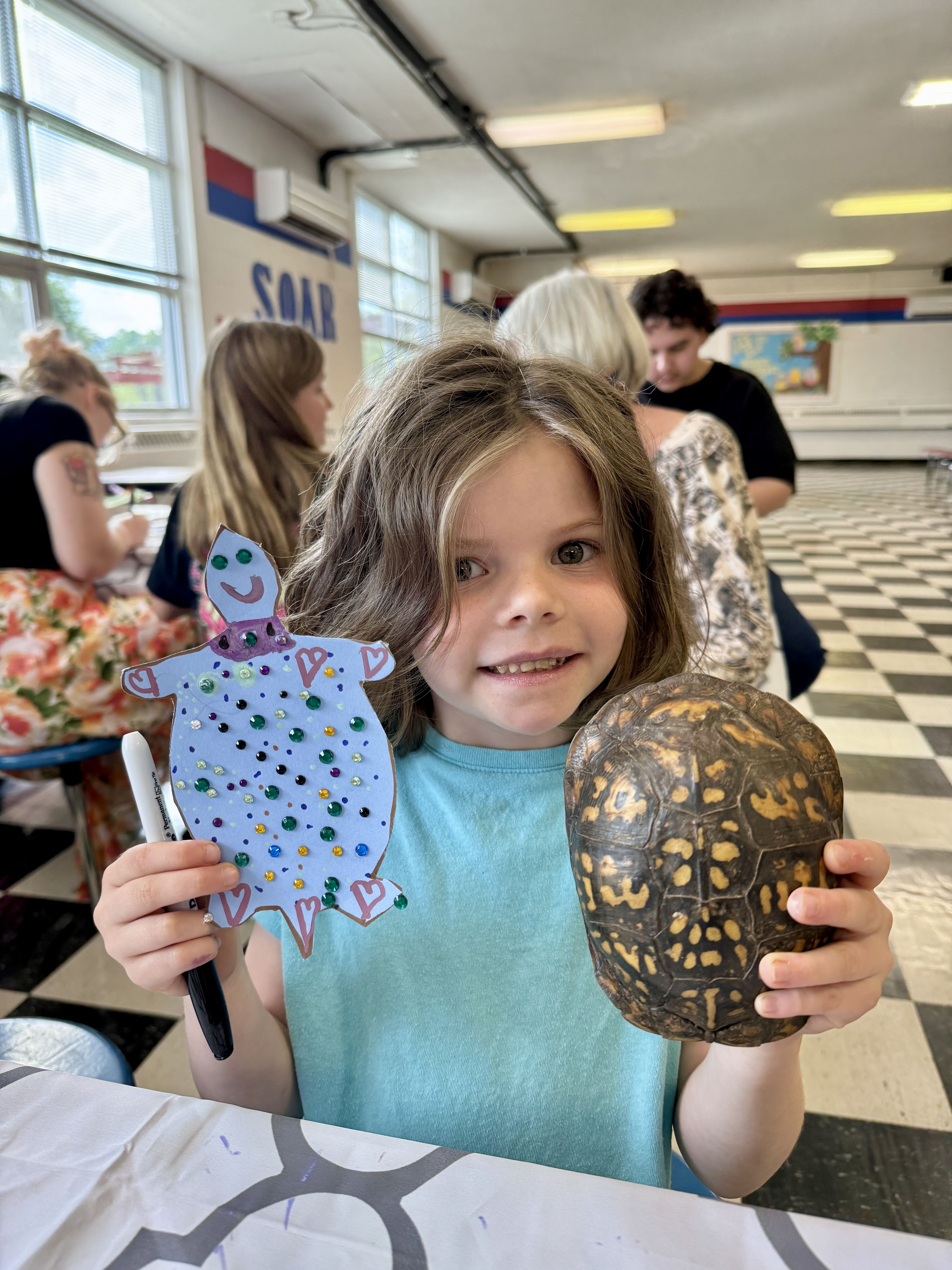 Smiling girl holding a turtle shell in one hand and her turtle inspired art in the other