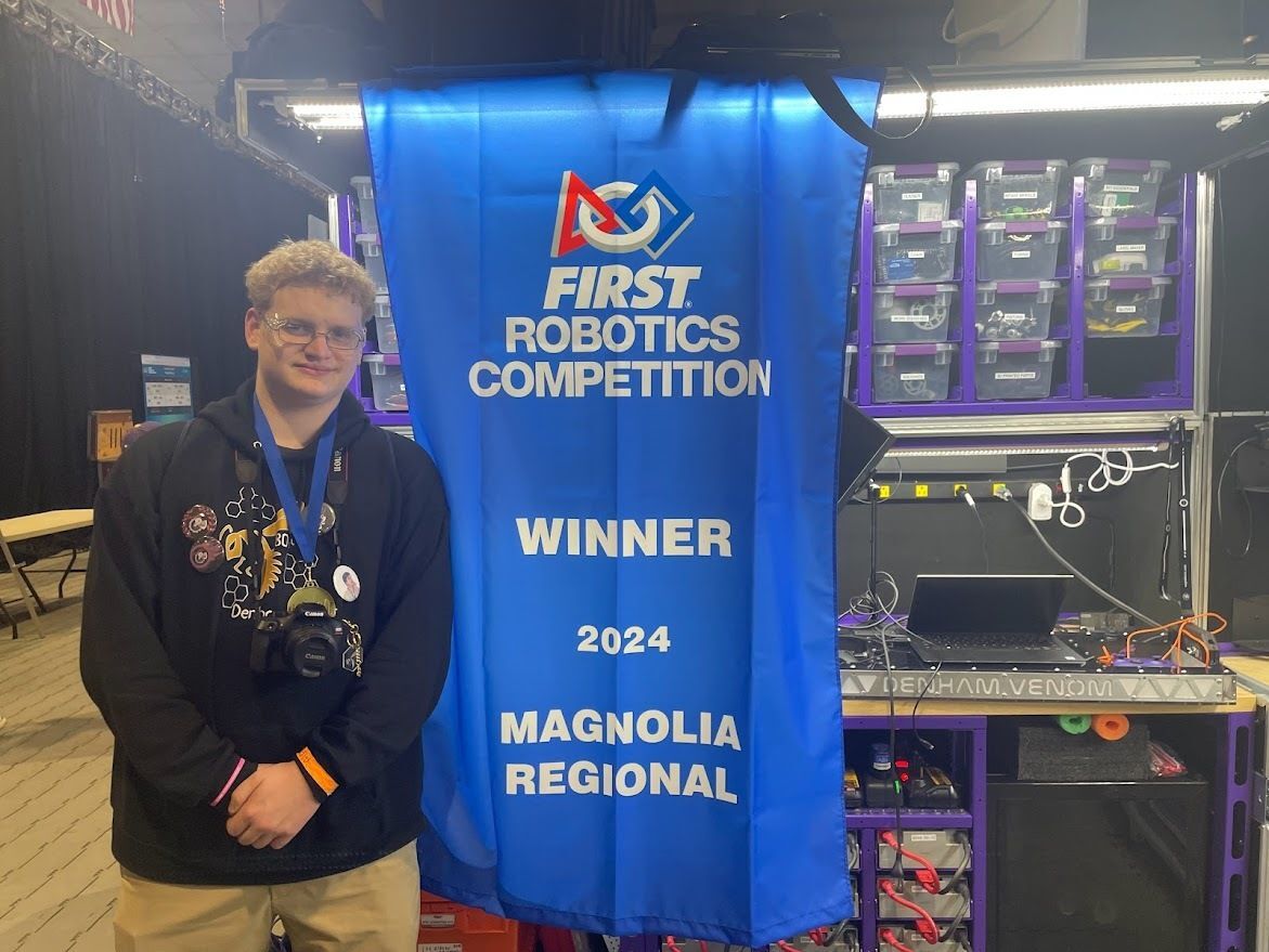 A student standing in front of a banner that states: FIRST Robotics Competition Winner 2024 Magnolia Regional