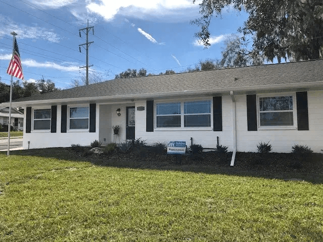 Single-story white Habitat for Humanity home with American flag and Habitat sign in front yard, representing affordable housing in Pasco County, Florida