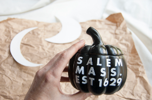 Black pumpkin with text: SALEM MASS. EST 16921, brown paper, paper crescent moon cut outs for DIY project.