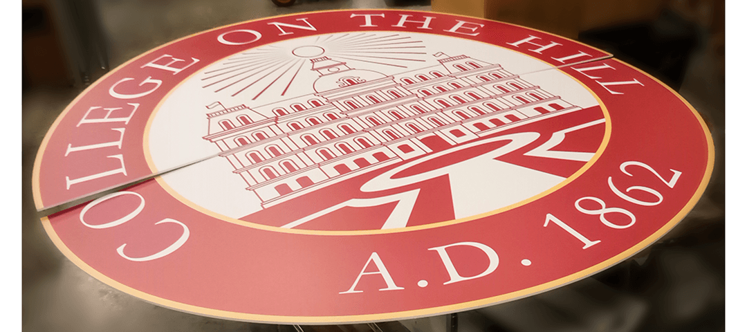 Large format printed circle PVC sign in two halves showing College on the Hill seal