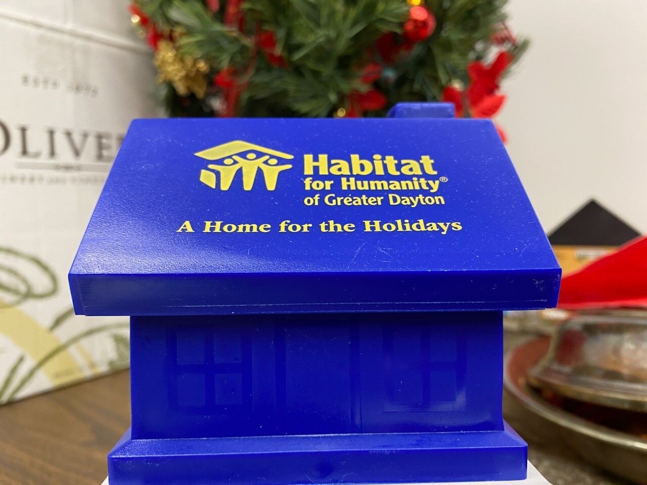 Blue plastic coin. bank shaped like a house. The bank bears the logo of Habitat for Humanity of Greater Dayton.