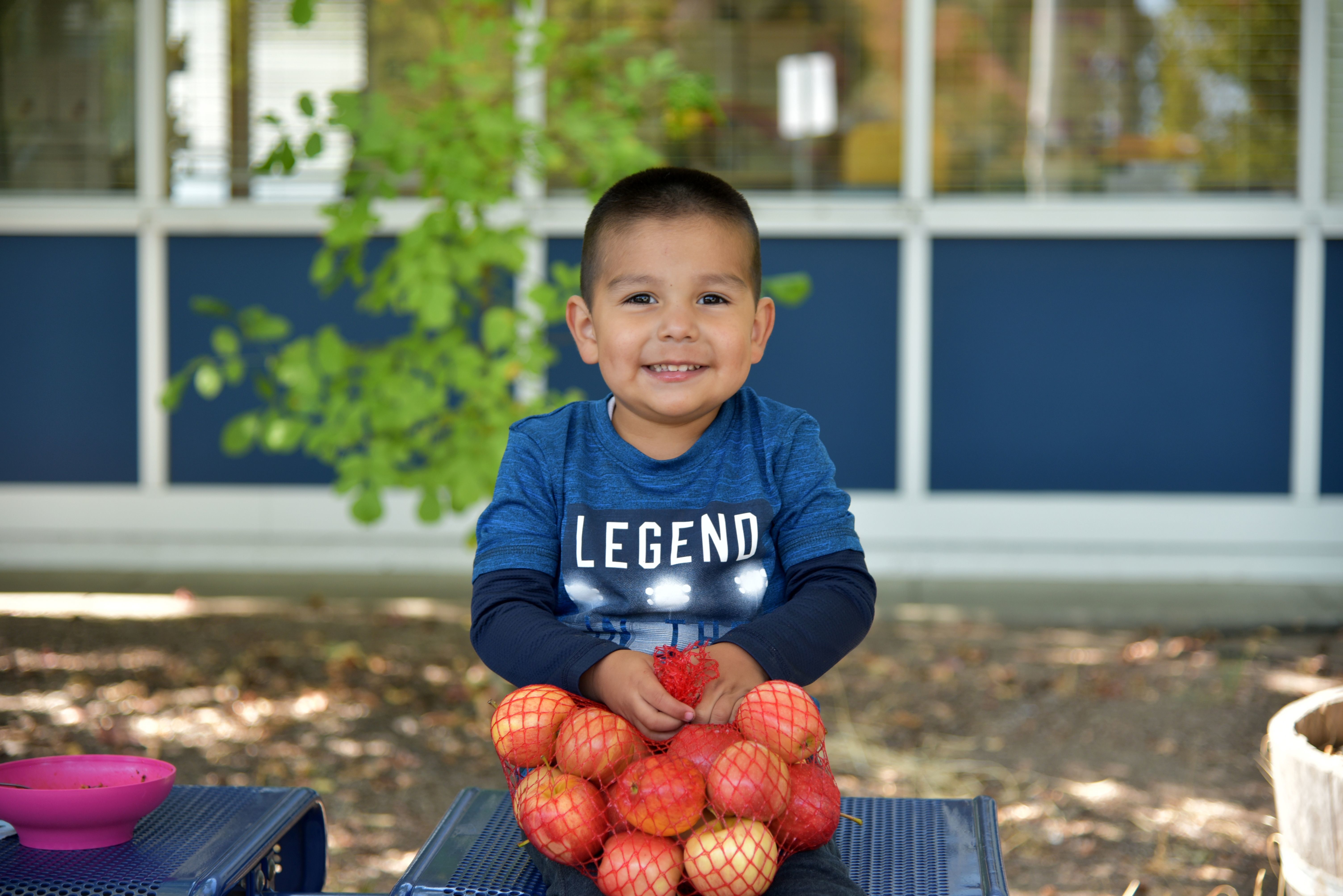 Young boy smiling and holding a bag of apples