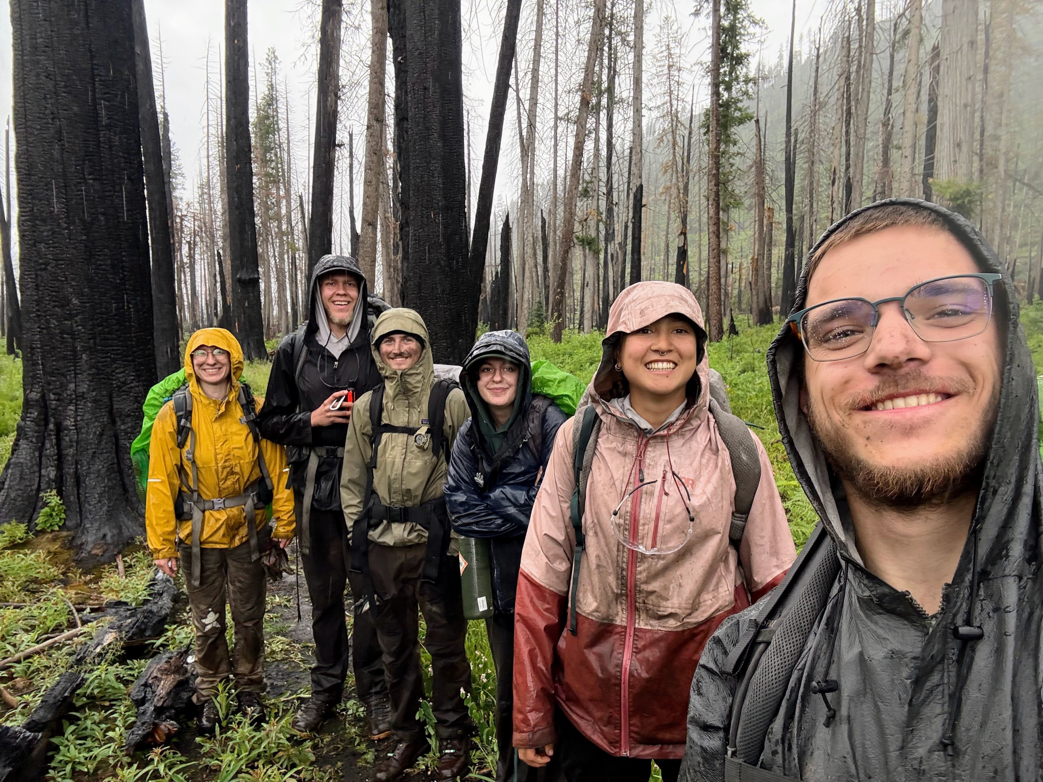A crew takes a selfie in the rain and standing among a burn area.