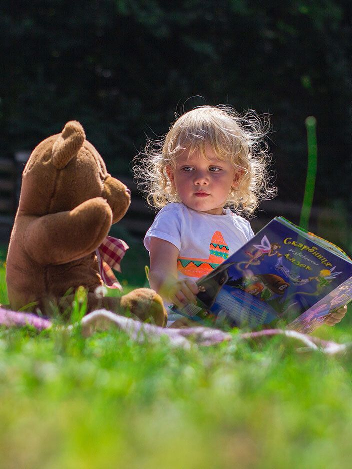 Young child reading a book with her teddy bear.