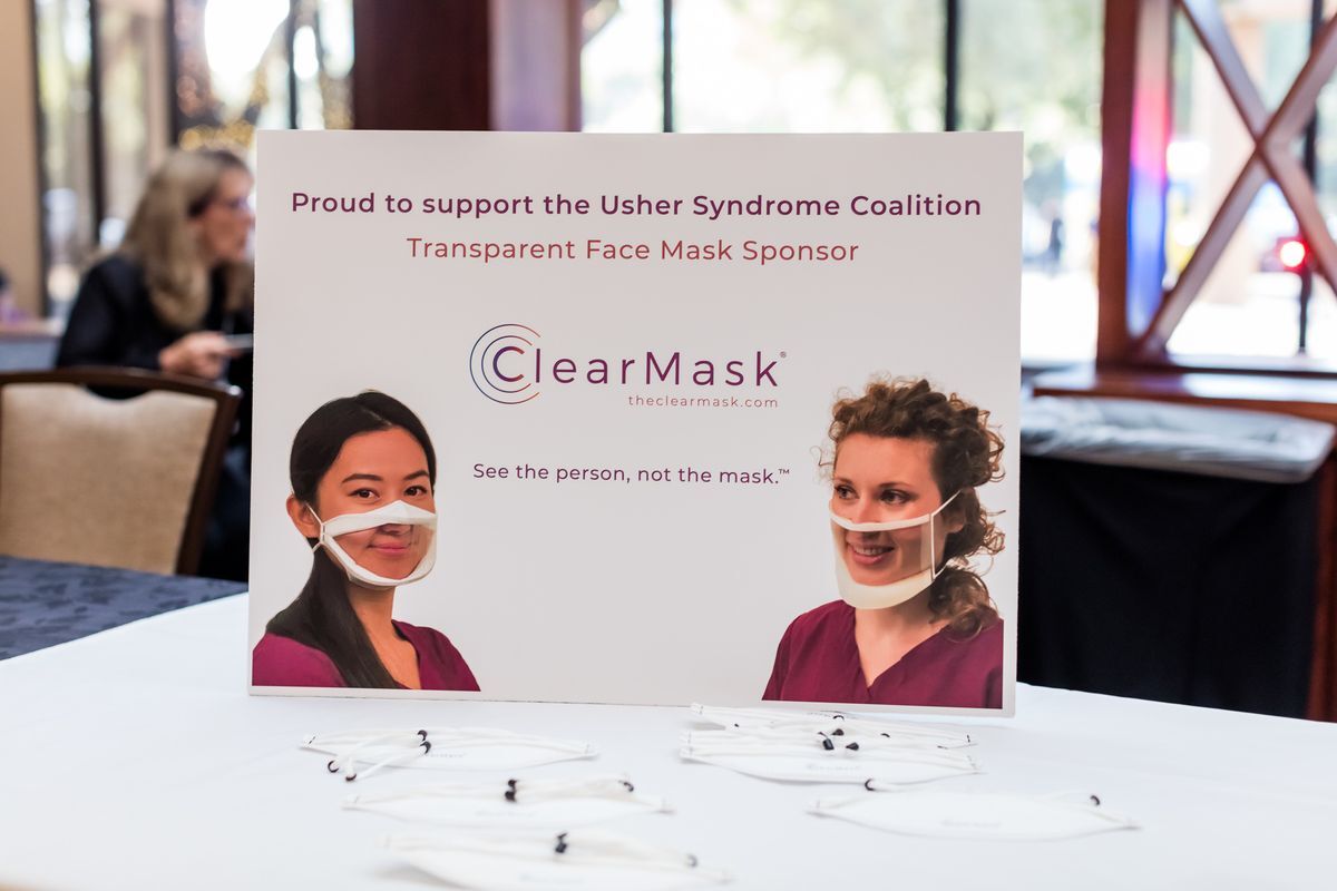 On a table is a sign advertising the brand ClearMask. A few samples of the product blend in with the table cloth. 
