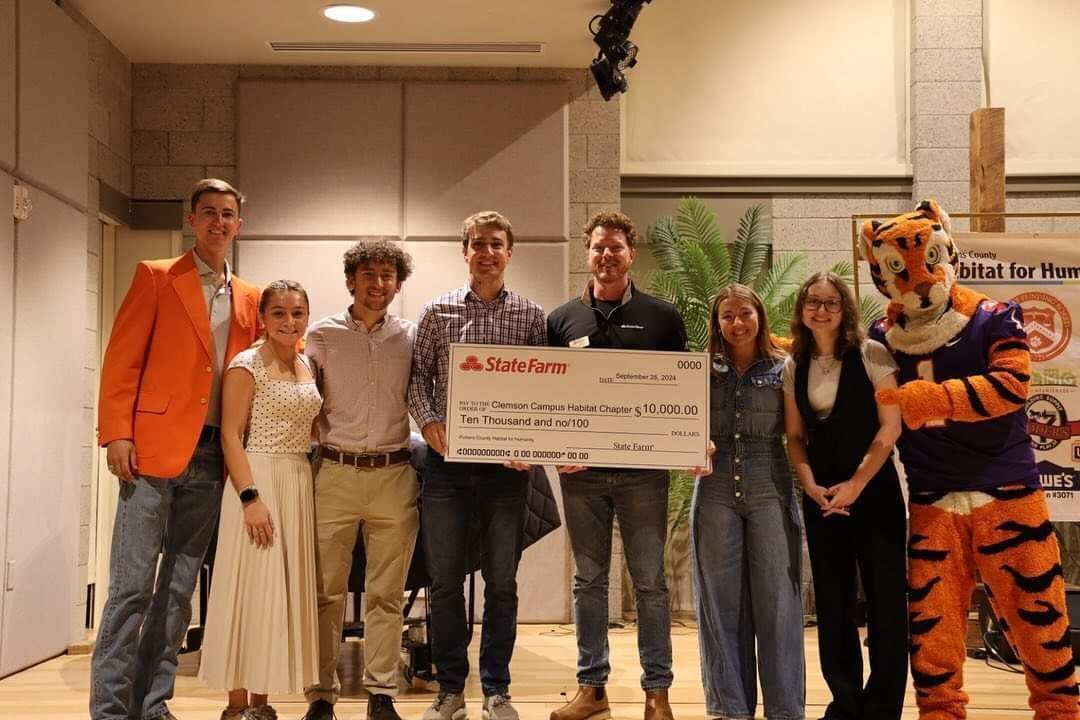 Daniel Webber, a State Farm representative and board member, presents a check to the Clemson Habitat for Humanity Campus Chapter, accompanied by the Clemson Tiger mascot. The check signifies State Farm's title sponsorship, showcasing their support.