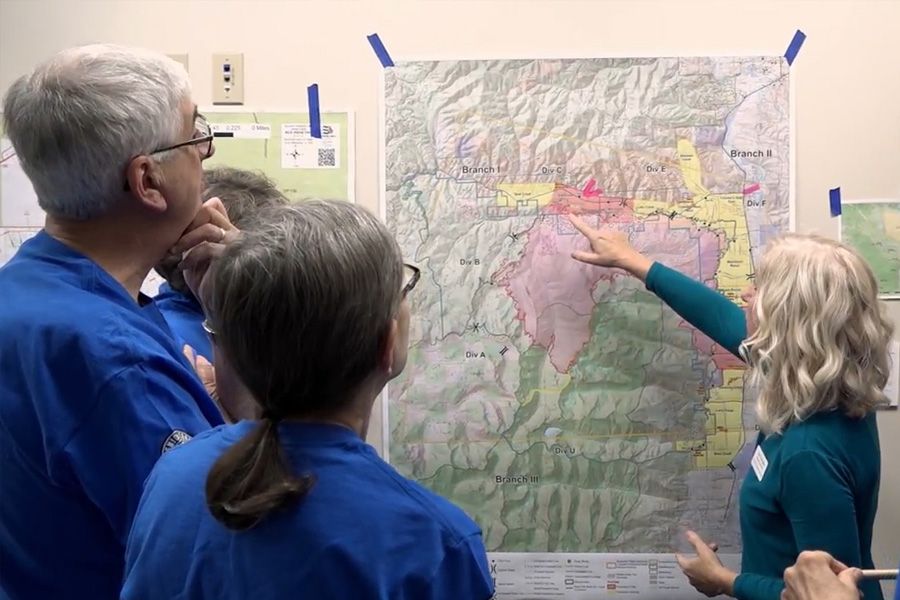 RSVP female volunteer coordinator pointing at map of Montana. Older adult volunteers looking at map at the Emergency Call Center.