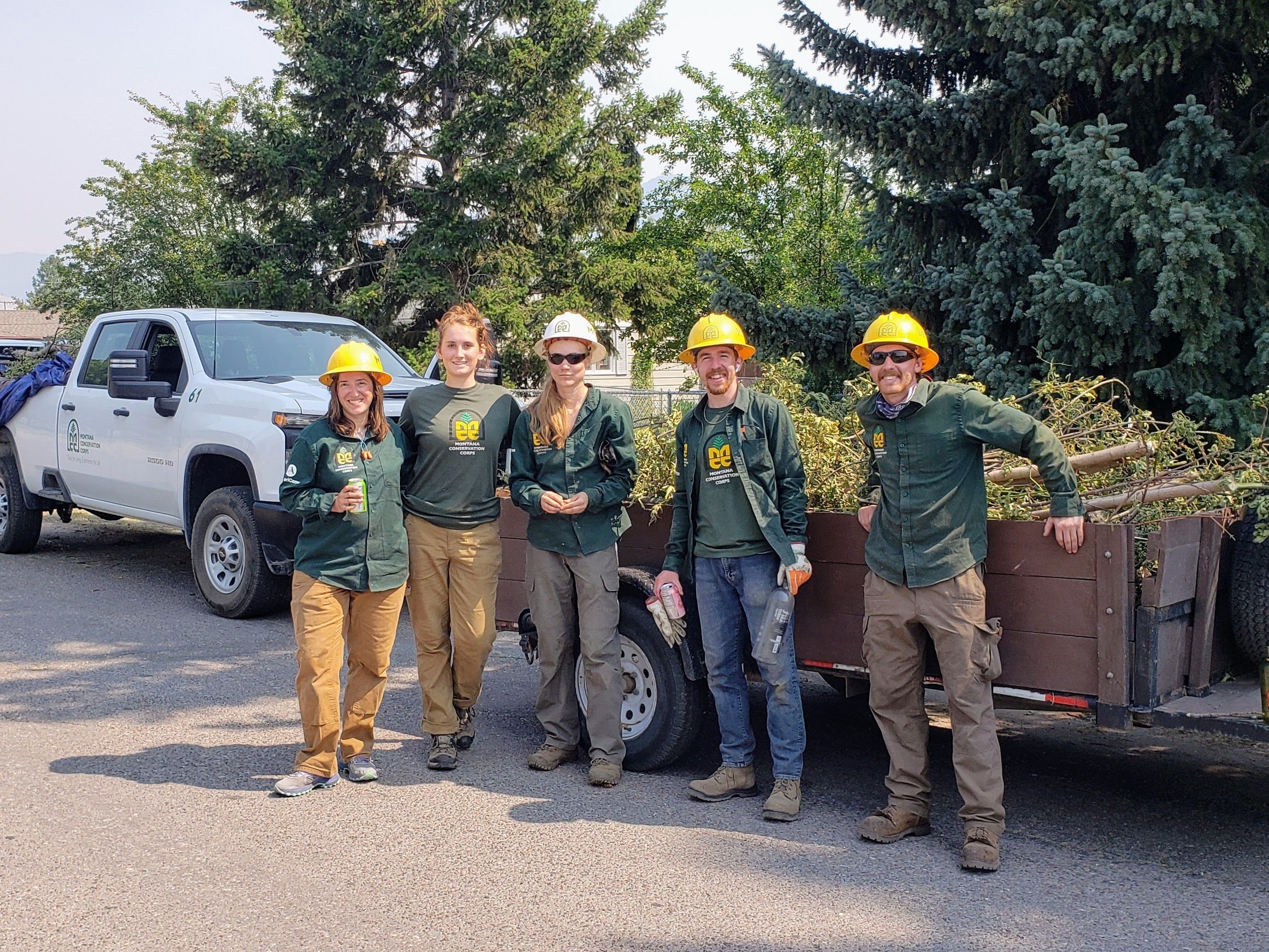 An MCC crew stands next to a trailer with storm debris in it.