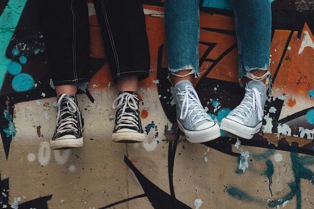 Teenagers wearing sneakers sitting on a wall marked with graffiti