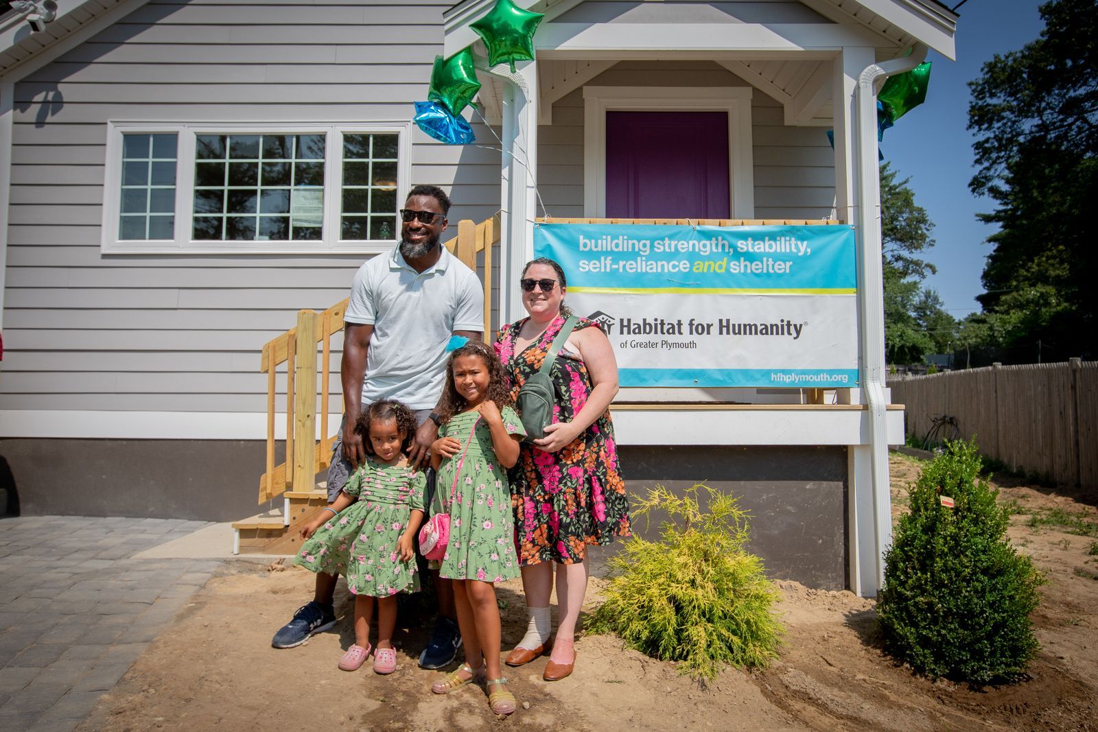 Family of four standing in front of their new home