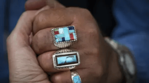 Two people hold hands, one with native turquoise rings on their fingers
