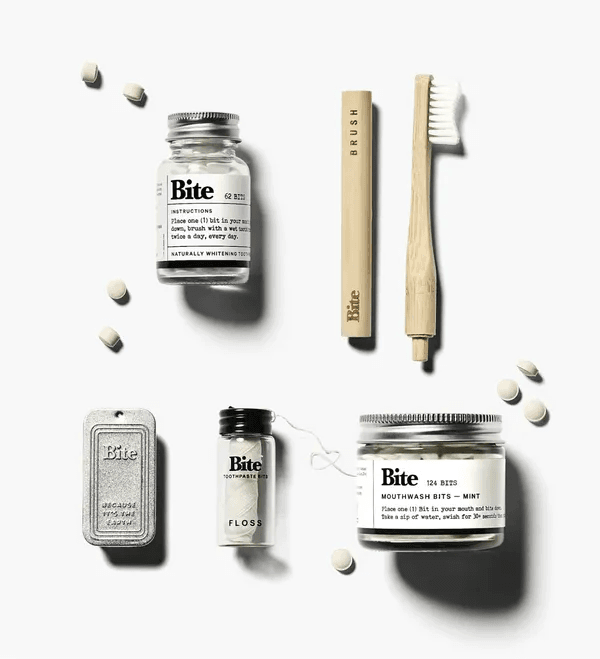 Bite toothpaste bits, bamboo brush, floss, and mouthwash bits in glass jars and metal tins, a creative packaging design idea for zero-waste brands.