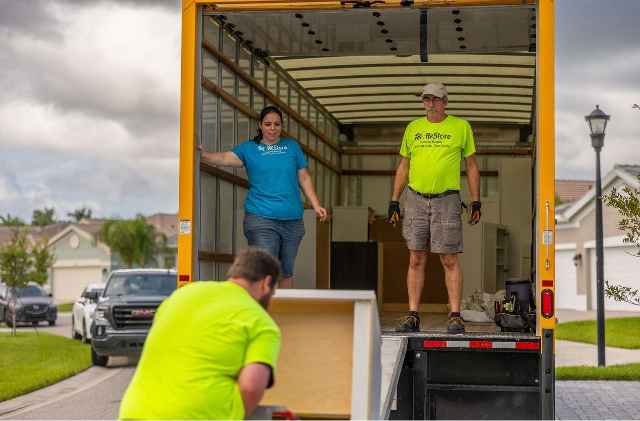 Habitat for Humanity ReStore donation pickup truck at a Pasco County home, with staff member loading a washing machine for free pickup in Zephyrhills, Florida
