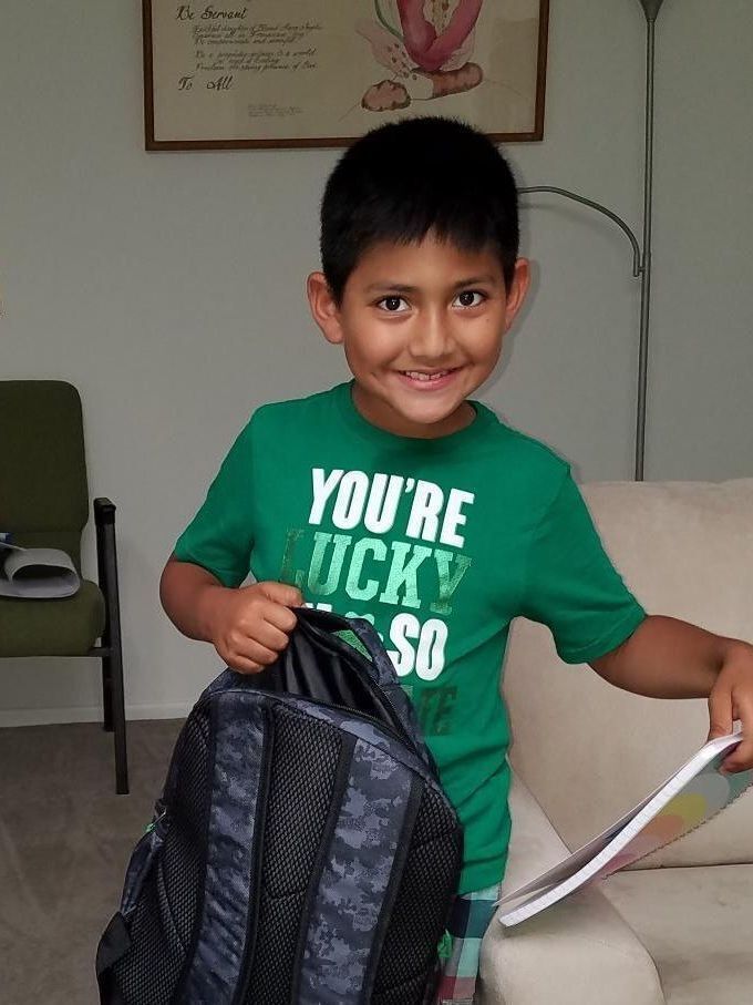 School aged boy holds a backpack.