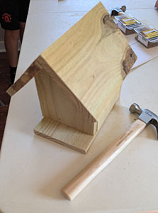 Finished wooden birdhouse on a table beside a hammer