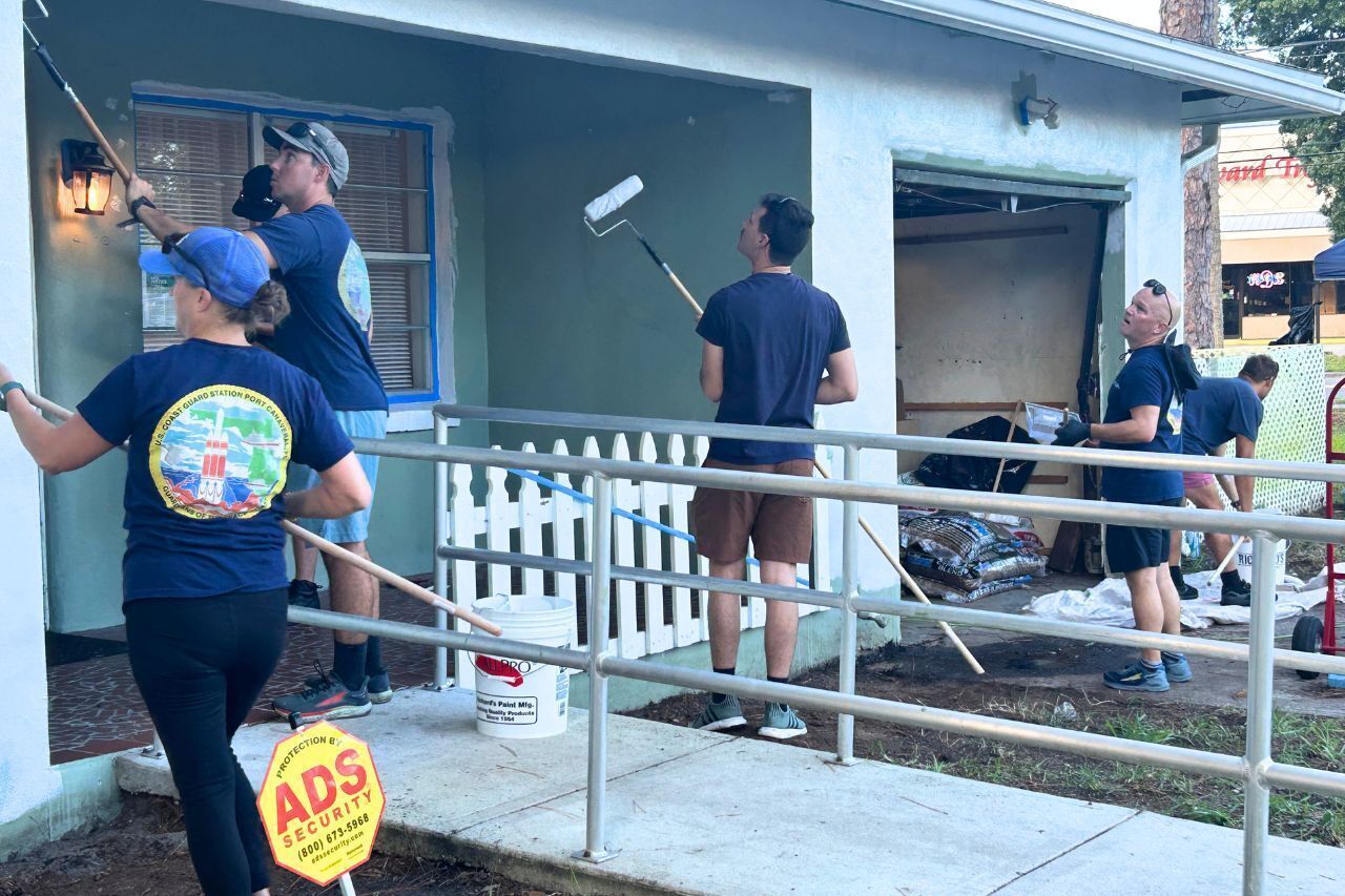 Volunteers paint the exterior of a house with rollers.