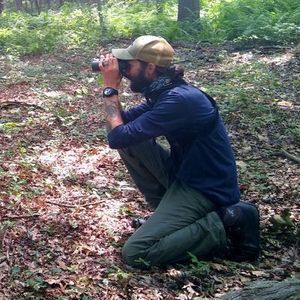 Charles Clarkson observing birds with binoculars in a forest